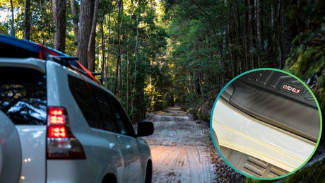 A white 4WD vehicle driving on a rugged dirt road through a dense forest. An inset close-up highlights a dent on the car's lower side panel, along with an 'OAD 4X4' badge on the floor mat.