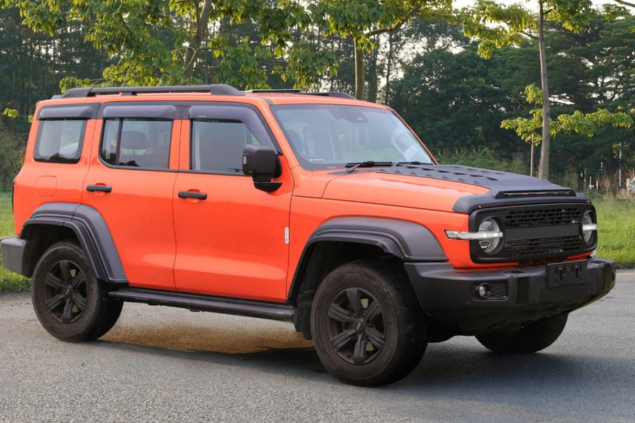 Orange 4WD SUV with black accents, featuring weather shields and rugged design, parked on a road with trees in the background